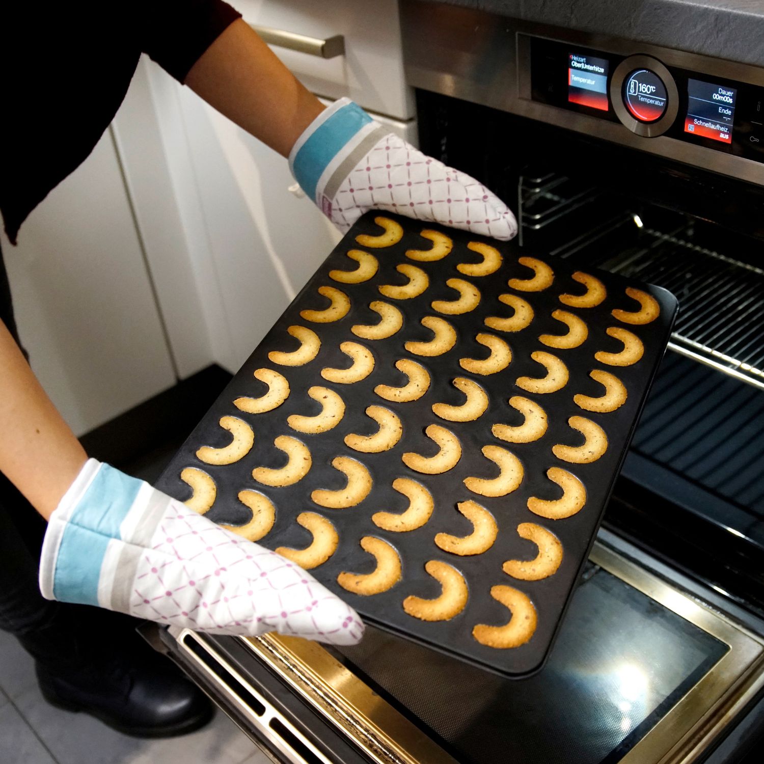 Vanillekipferl-Backblech mit fertigen Vanillekipferln wird aus dem Backofen genommen