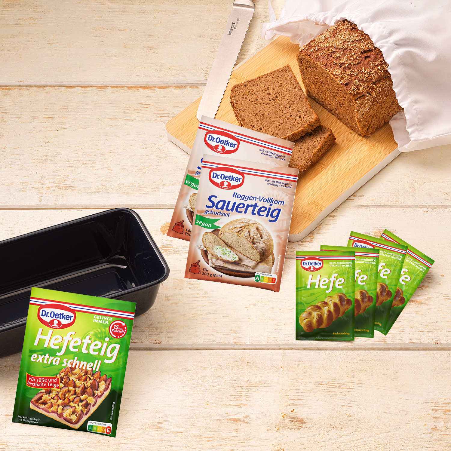 Gebackenes Brot auf einem Holzbrett zum teilm im Baumwollbeutel mit dazu passenden Zutaten zum Brot backen und einer Backform