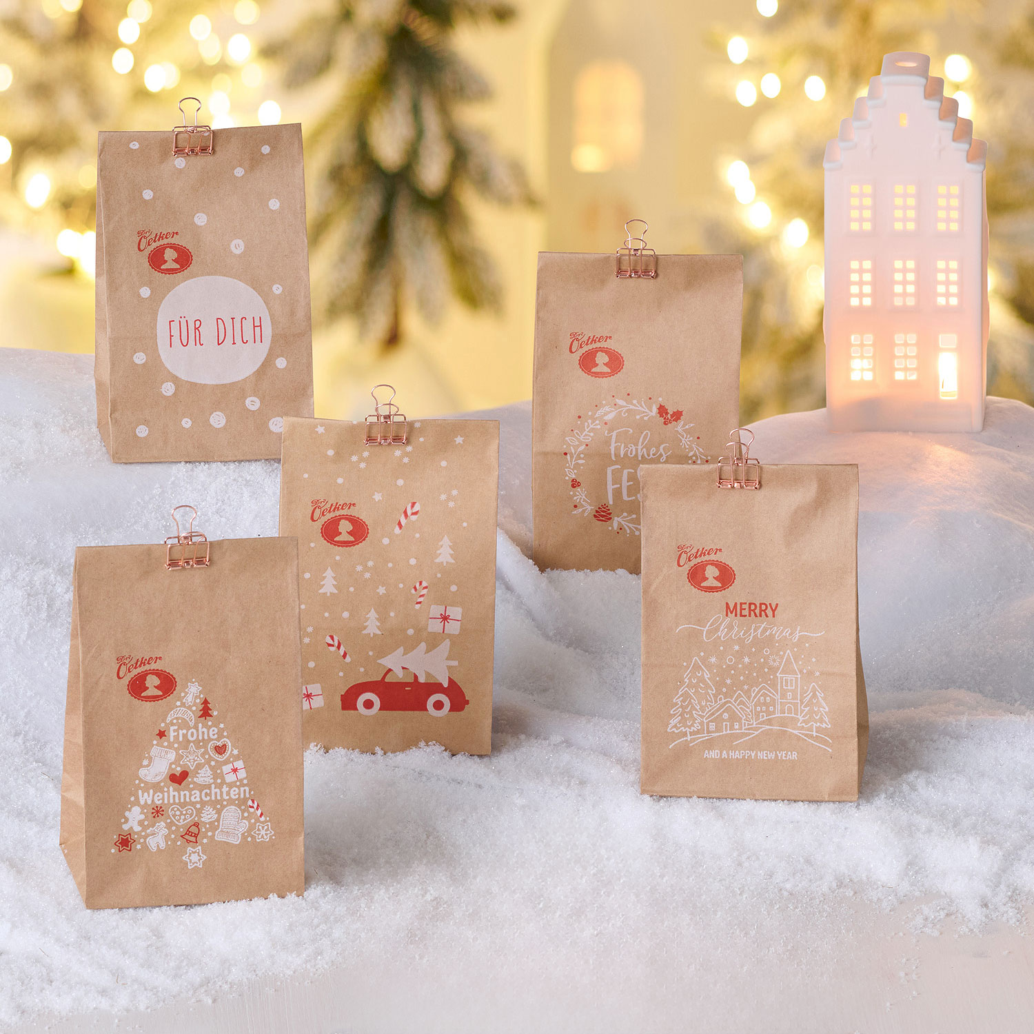 Kekstüten von Dr. Oetker mit weihnachtlichen Motiven als Stimmungsbild vor Hintergrund mit weißen Miniäusern und Tannen