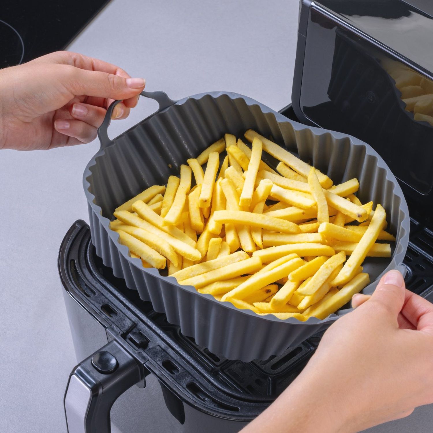 Eine eckige Silikonform gefüllt mit Pommes, die in eine Heißluftfritteuse gelegt wird