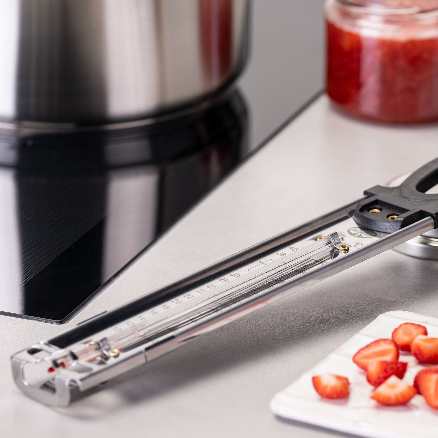 Zuckerthermometer, das auf Kuechenplatte liegt, daneben Erdbeeren auf einem Brettchen