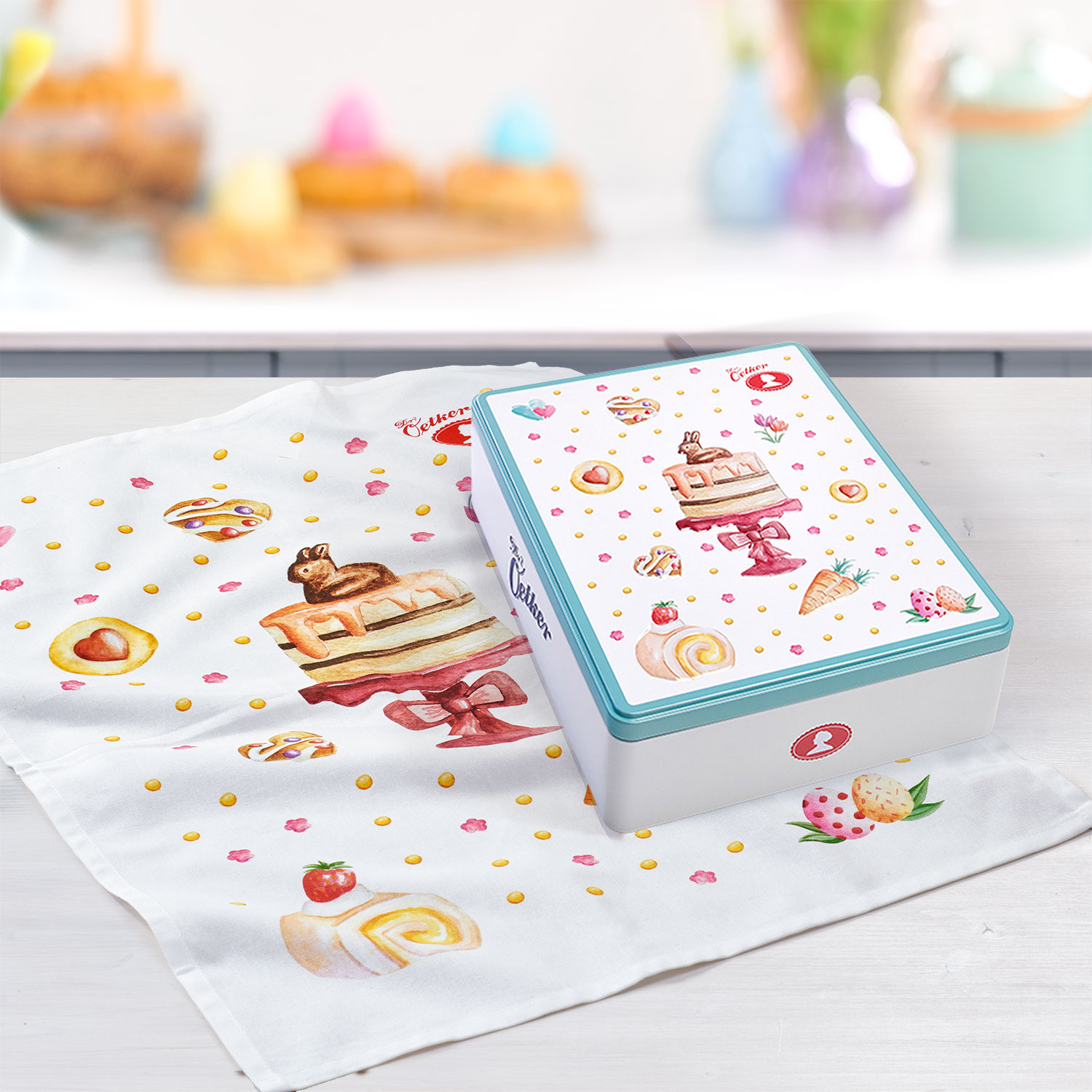 Geschenk-Set aus Keksdose und Geschirrtuch mit österlichem Motiv vor Küchenhintergrund
