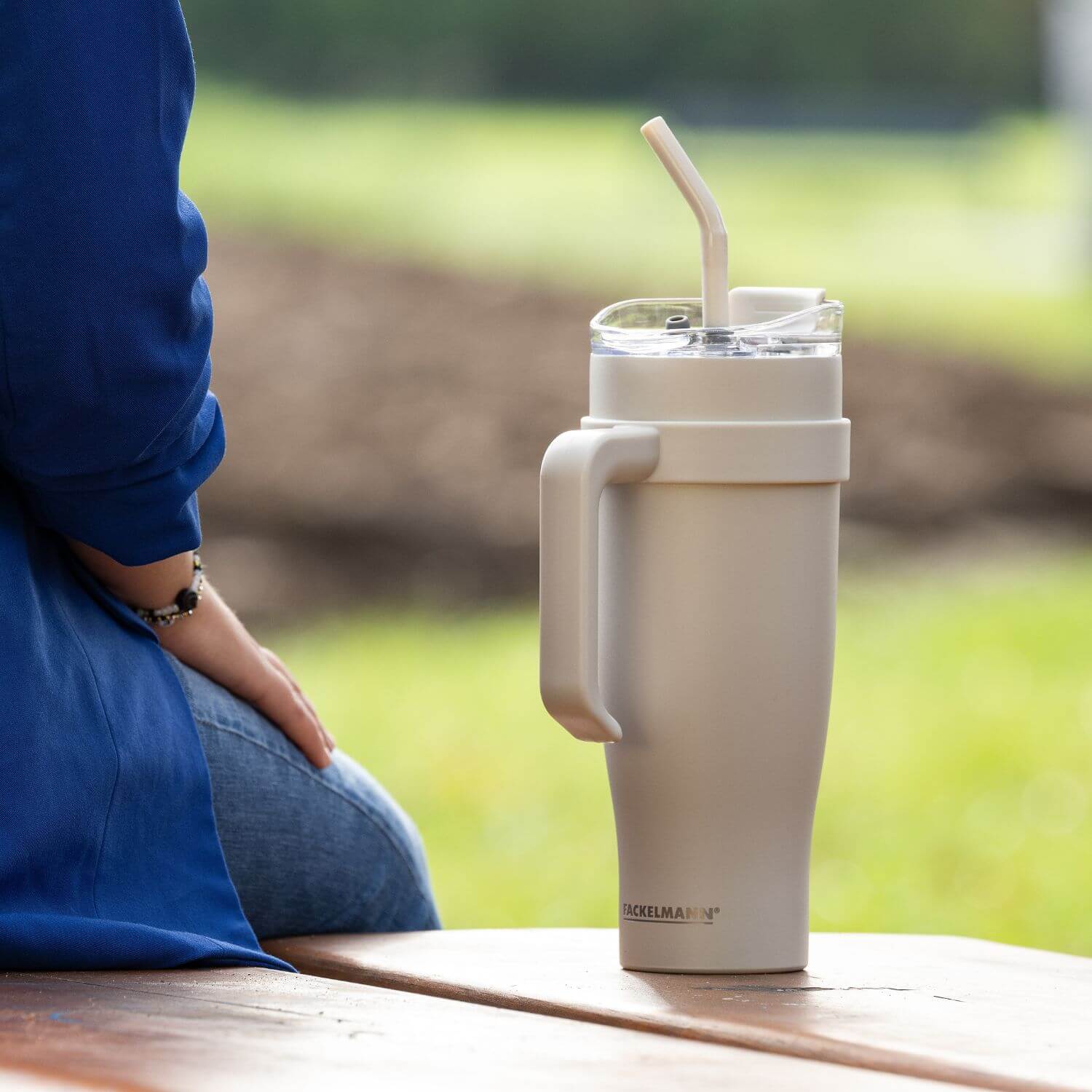 Isoliertrinkbecher beige XXL auf einer Bank neben einer sitzenden Person