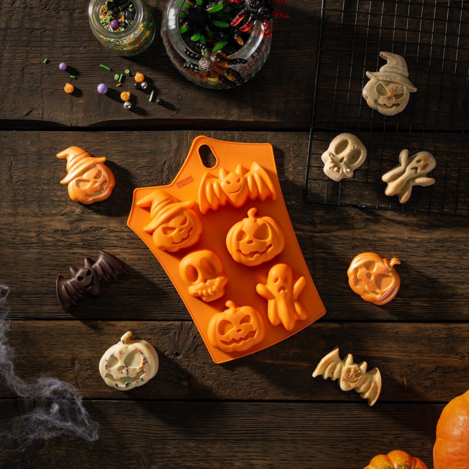 Minikuchenform für Schokolade in Halloweenmotiven neben Schokolade aus der Form auf dunklem Holzhintergrund