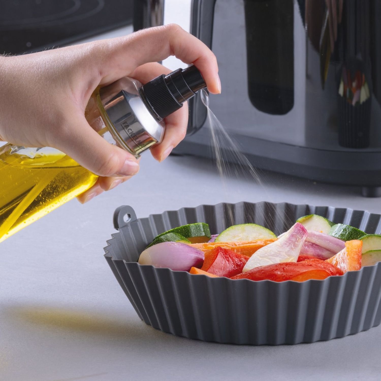 Eine runde Silikonform, befüllt mit Gemüse das mit Öl besprüht wird