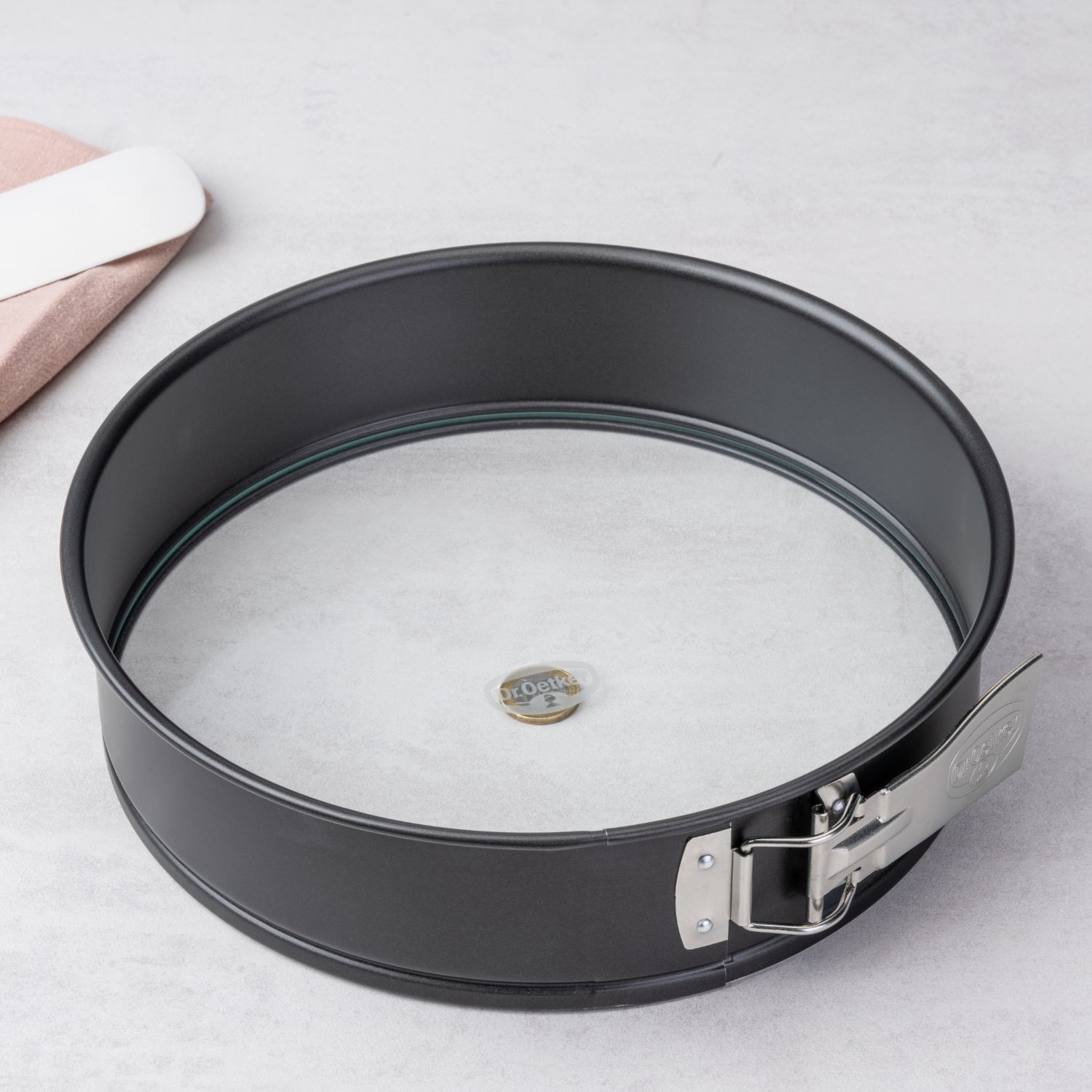 Eine schwarze Springform mit Glasboden, stehend auf einer Ein-Euro Münze