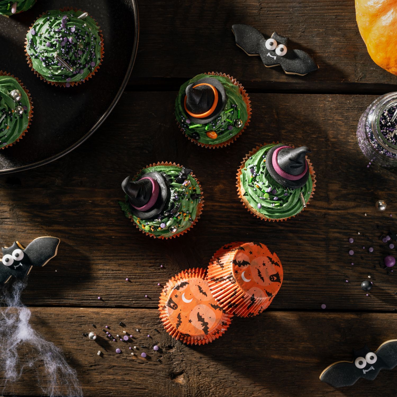 Orangene Halloween-Papaierbackfoermchen von oben neben Halloween-Cupcakes