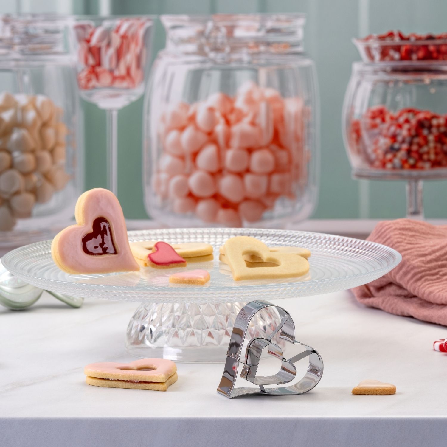 Moodbild des 2in1 Ausstechers Linzer Herz vor drapierten Süßigkeiten und Plätzchen im Hintergrund