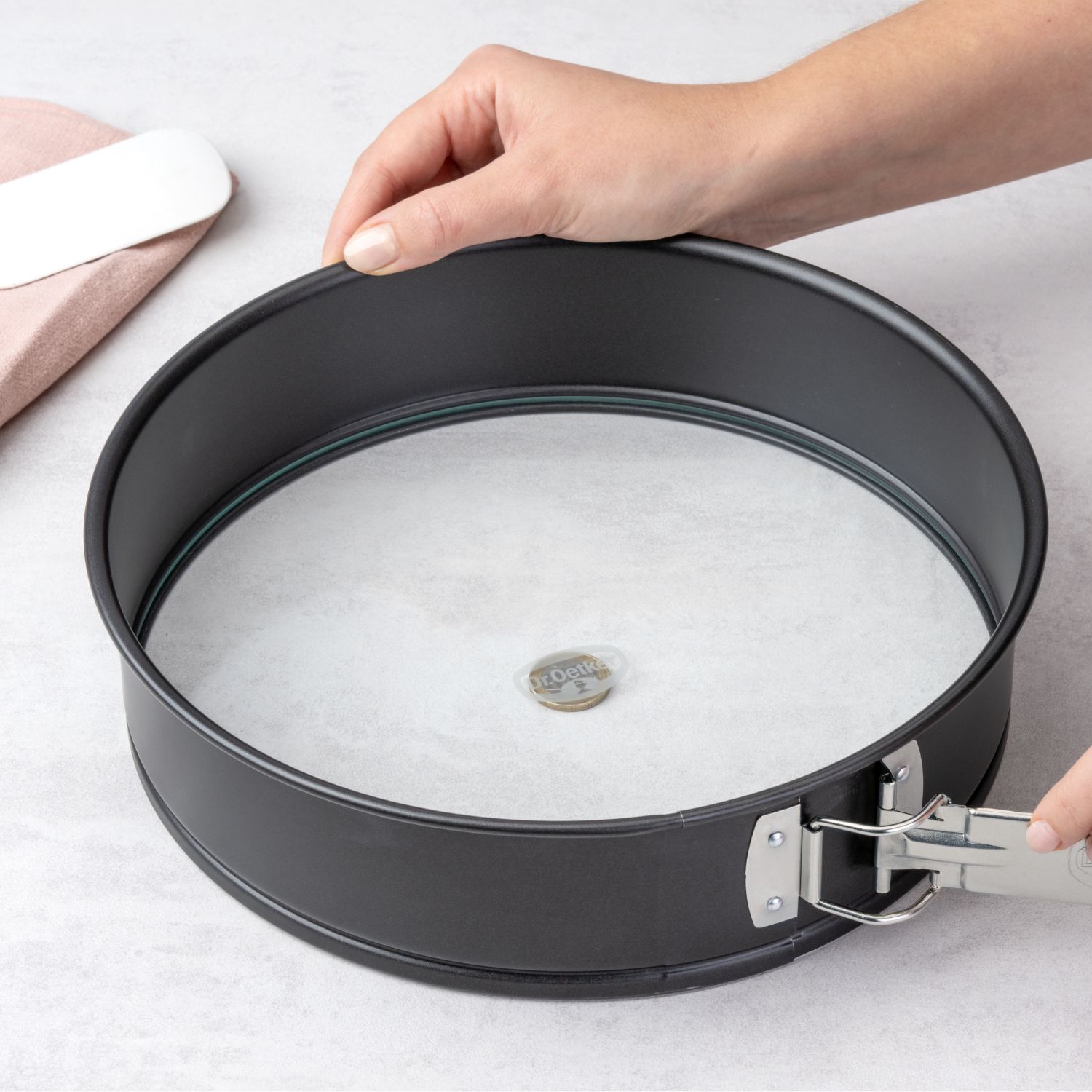 Eine schwarze Springform mit Glasboden die gerade geöffnet wird