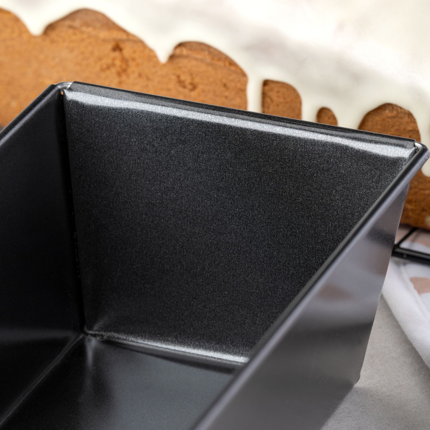 Eine Nahaufnahme der Kanten der schwarzen Kasten-Backform, mit einem Kuchen im Hintergrund