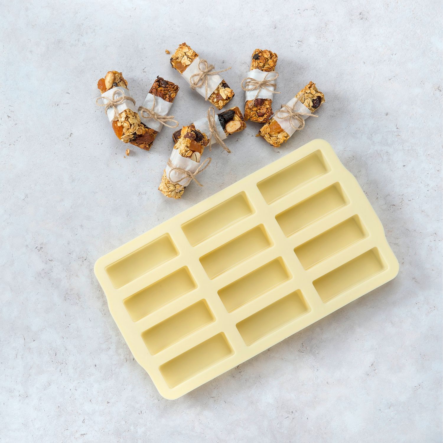 Eine gelbe Silikonform für Minikuchen oder Müsliriegel von oben, daneben liegen Müsliriegel
