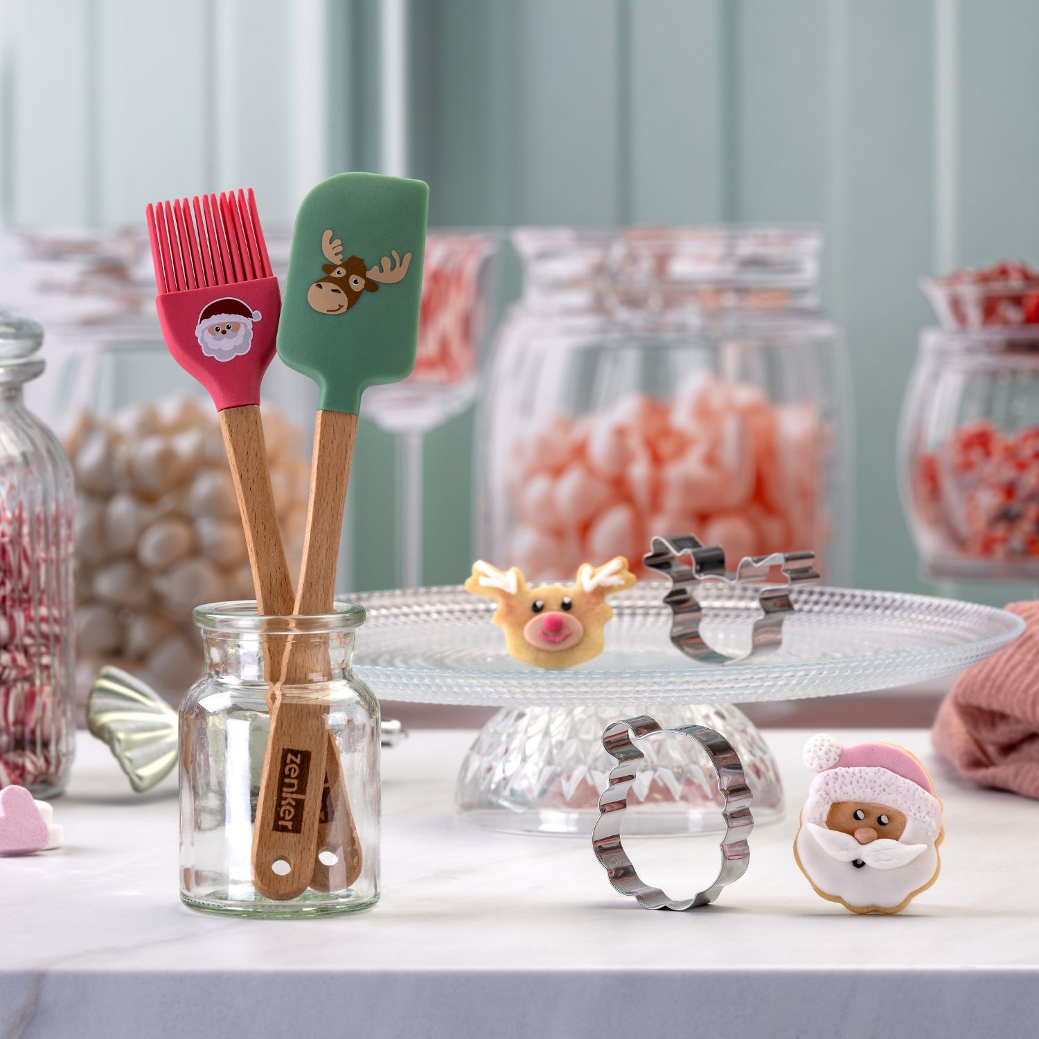 weihnachtliche Backhelfer mit weihnachtlichem Motiv und passenden Ausstechern vor dekorativem Hintergrund aus Süßigkeiten