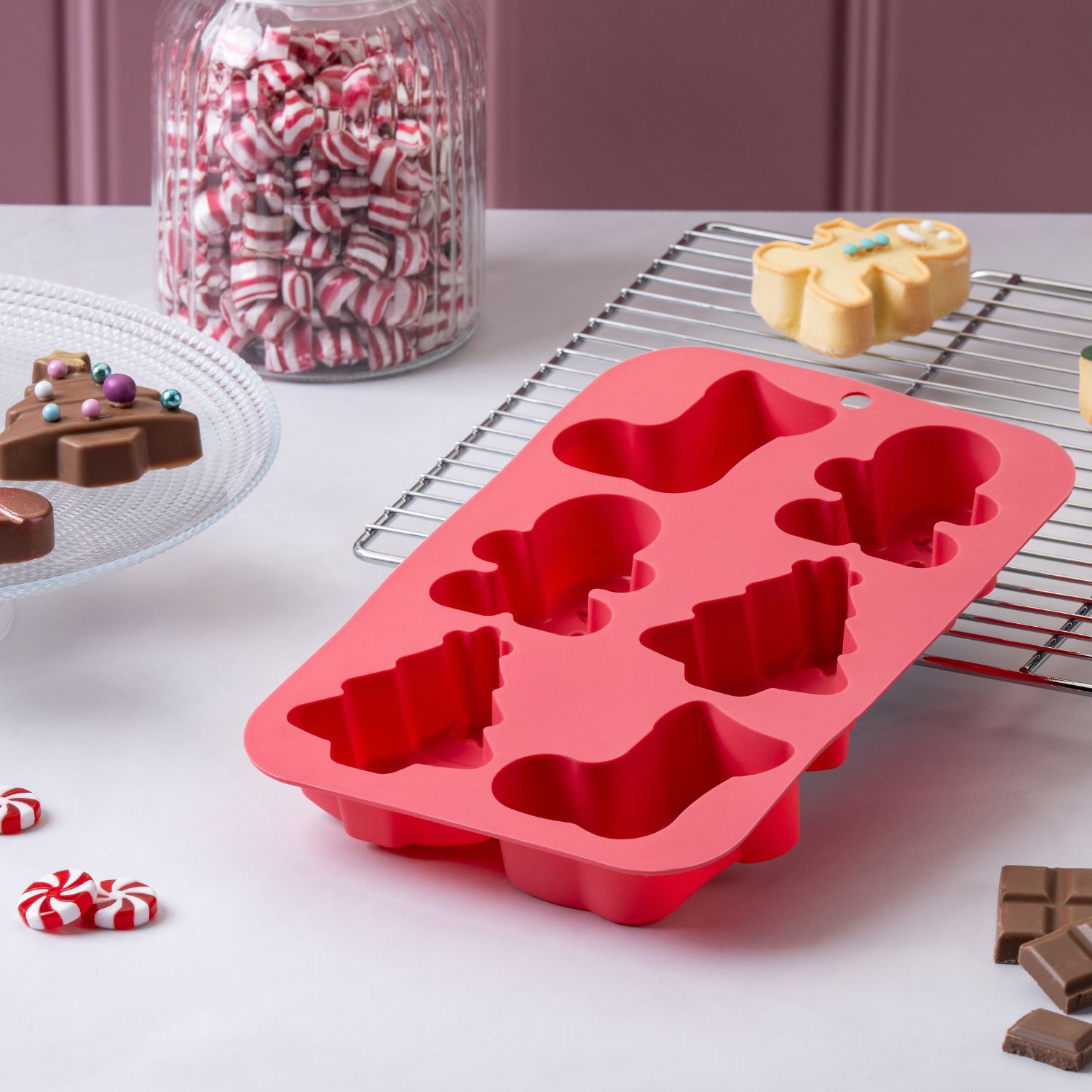 Weihnachtsrote Siilikonform für Gebäcke mit weihnachtlichen Motiven vor dekorativem Hintergrund mit Kuchenrost