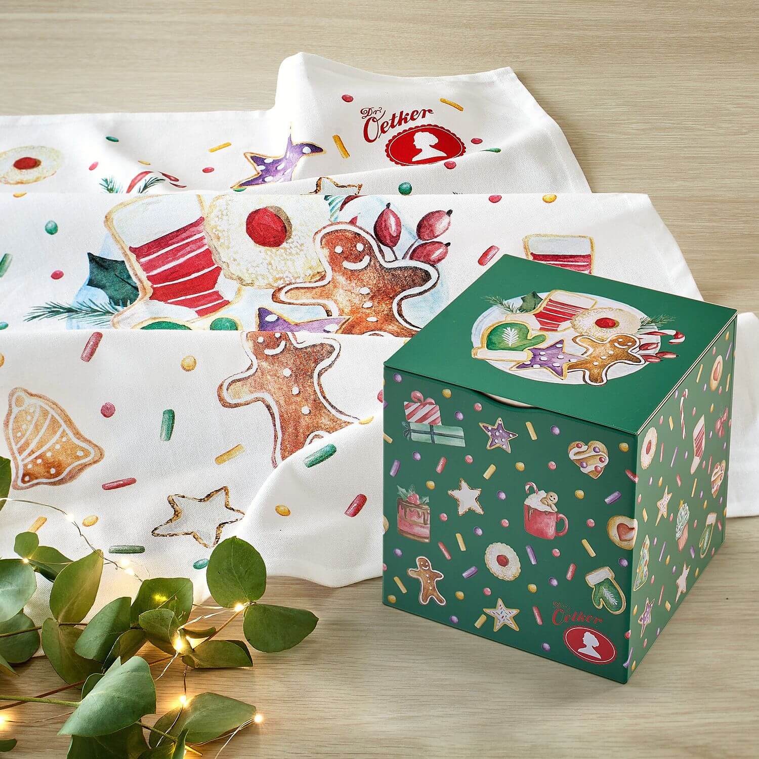 Grüne Keksdose und Geschirrtuch mit Weihnachtsmotiven  auf Holzplatte