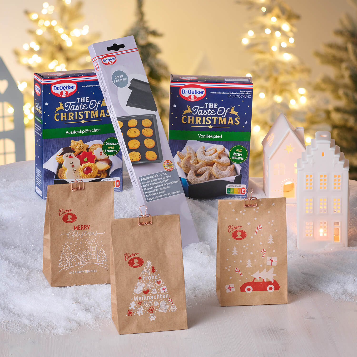 weihnachtliche Kekstüten und weihnachtliche Backmischungen vor weihnachtlichem Hintergrund mit Schnee und einem Backblech von Dr. Oetker