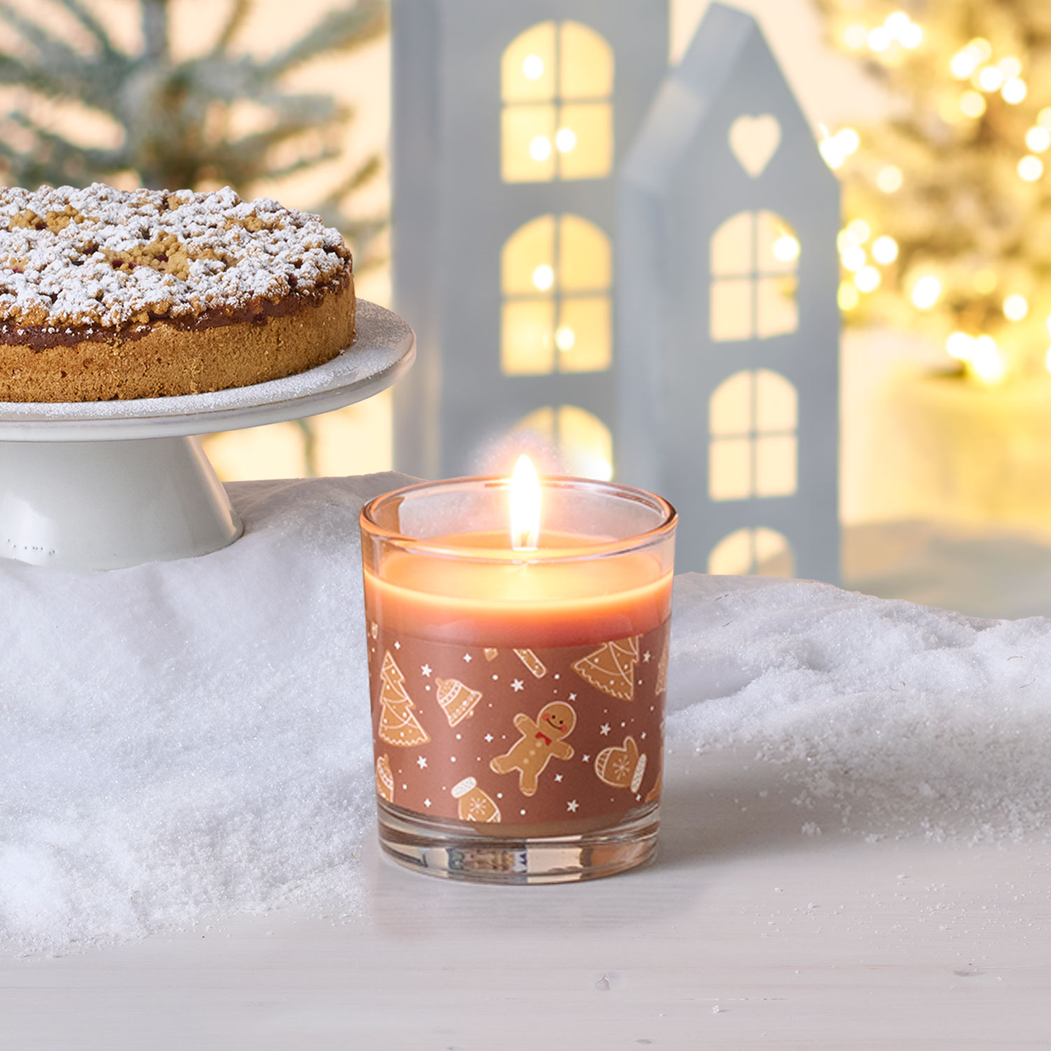 Eine angezündete Duftkerze mit Lebkuchen-Geruch, weihnachtlicher Hintergrund und Kuchen