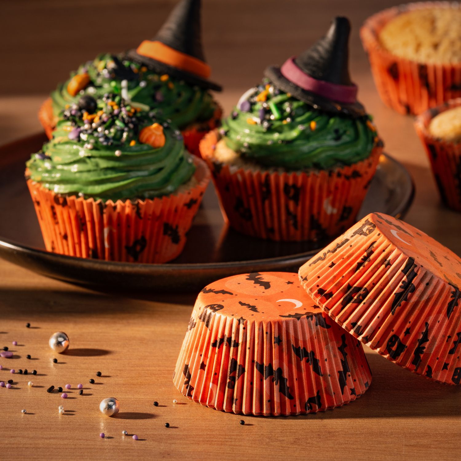 Orangene Papiermuffinförmchen auf einer Holzplatte vor Halloween-Gebäck