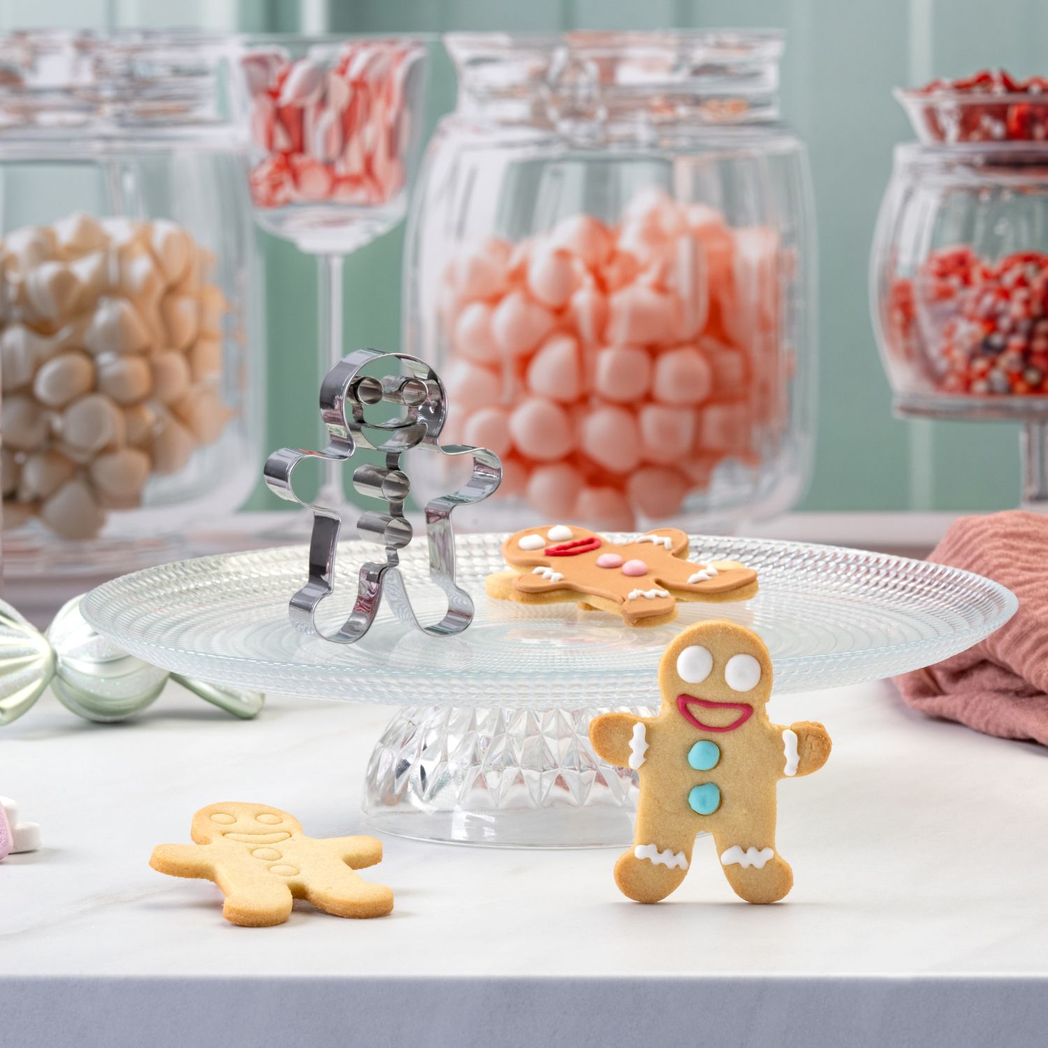 Weihnachtlicher Prägeausstecher Lebkuchenmann vor dekorativem Hintergrund mit fertigen Plätzchen und Süßigkeiten